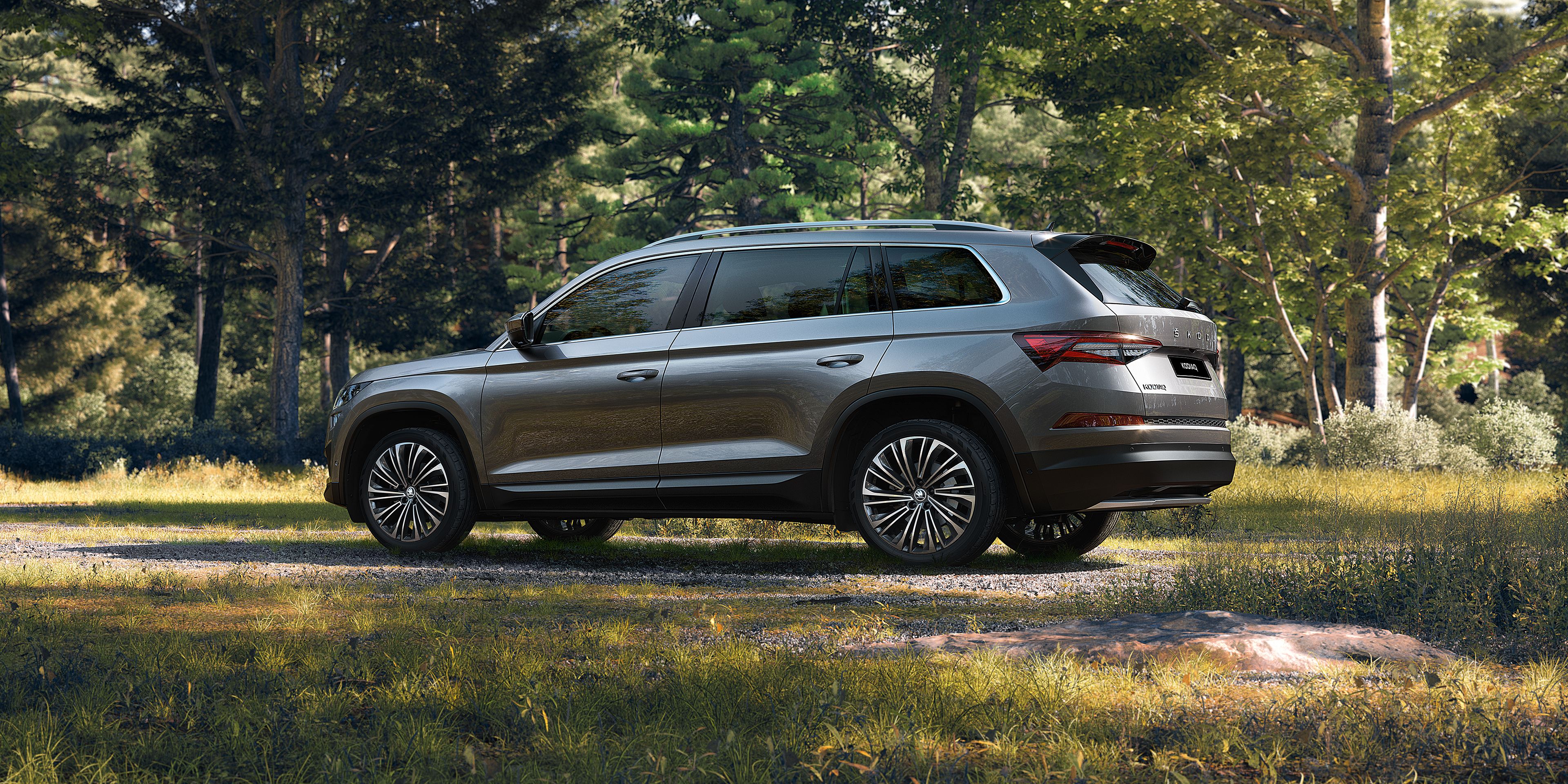 Eine Frau und ein Junge stehen neben dem Kofferraum eines Škoda Kodiaq. Dahinter sieht man einen Fluss und Berge
